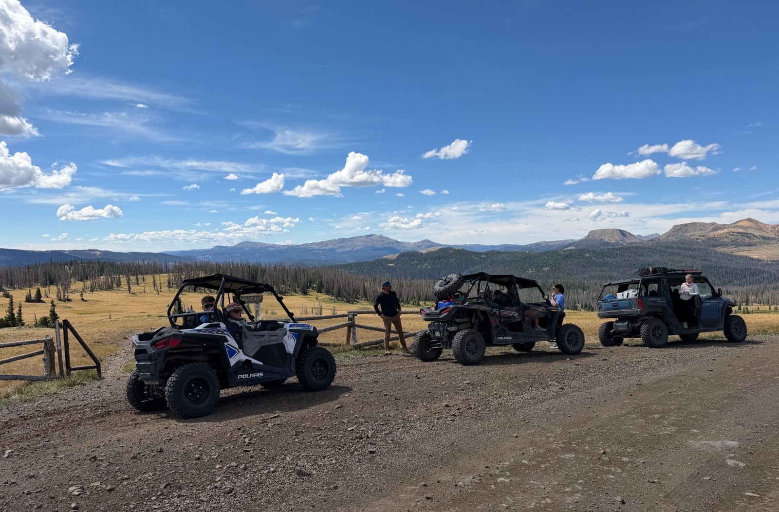UTVs staged at a trailhead overlooking a wide alpine valley