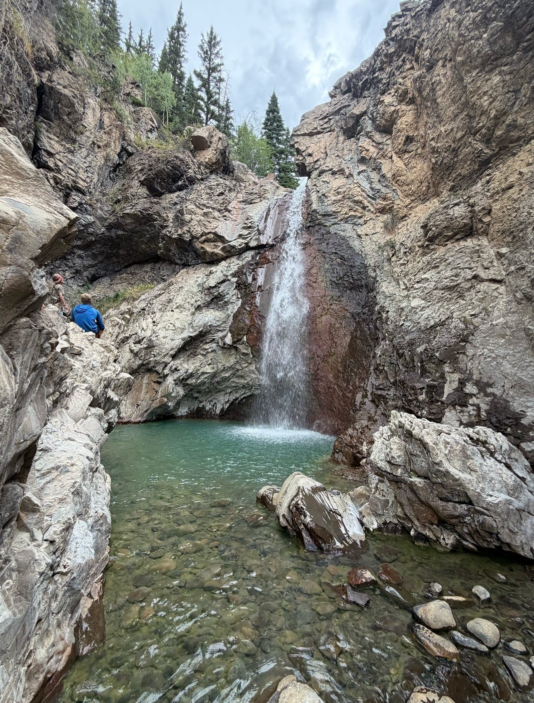 A hidden waterfall pouring into a turquoise pool in a rocky canyon near Del Norte